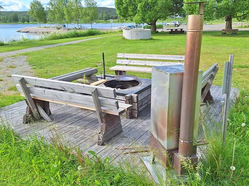 Eine gemauerte Feuerstelle mit Holzbänken am Ufer.